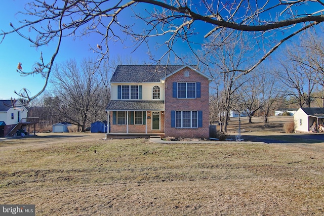 traditional-style house featuring covered porch, a storage unit, an outdoor structure, a front yard, and brick siding