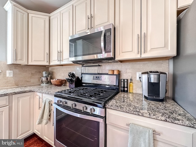 kitchen with appliances with stainless steel finishes, white cabinetry, light stone counters, and tasteful backsplash