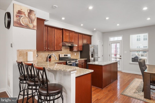 kitchen featuring a kitchen island, under cabinet range hood, hardwood / wood-style floors, decorative backsplash, and appliances with stainless steel finishes