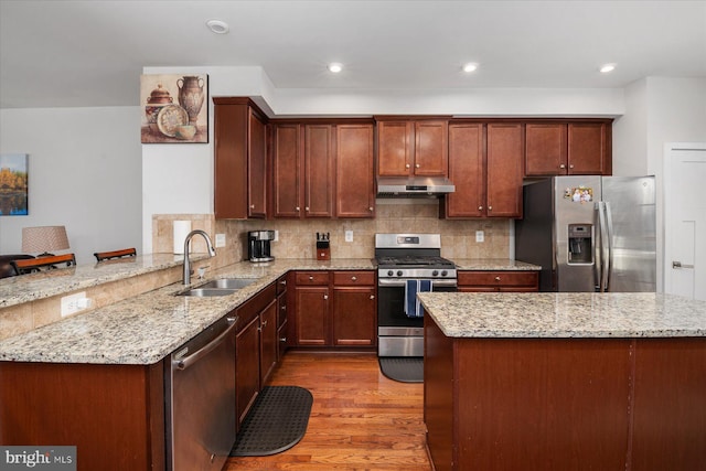 kitchen with light stone counters, dark wood-style floors, a sink, stainless steel appliances, and under cabinet range hood