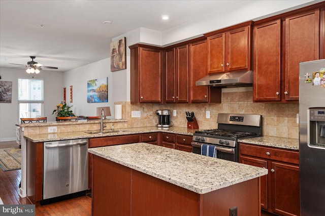 kitchen featuring under cabinet range hood, a sink, backsplash, stainless steel appliances, and a peninsula