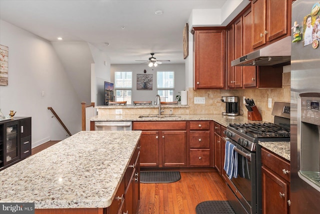 kitchen featuring a sink, under cabinet range hood, tasteful backsplash, wood finished floors, and stainless steel appliances