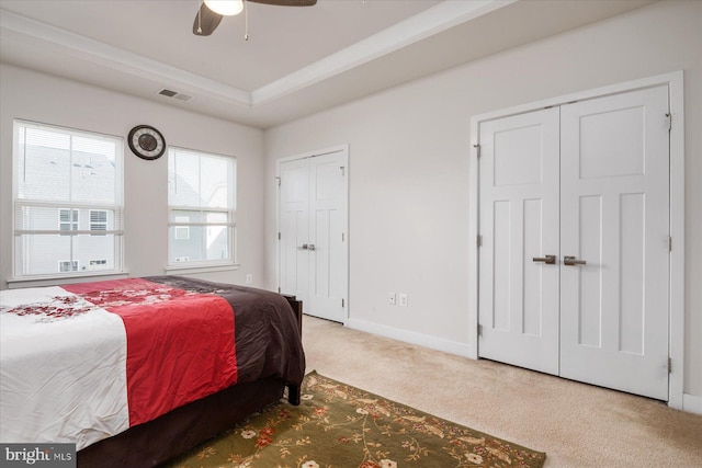 bedroom featuring visible vents, baseboards, a tray ceiling, multiple closets, and carpet flooring