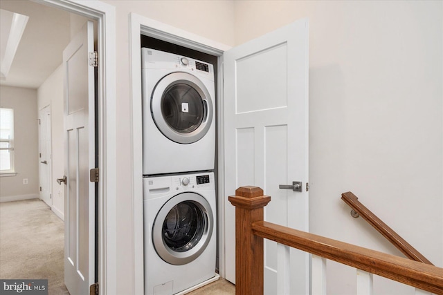 clothes washing area with stacked washer / drying machine, baseboards, light colored carpet, and laundry area