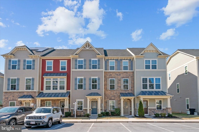 townhome / multi-family property with a standing seam roof, uncovered parking, stone siding, and metal roof