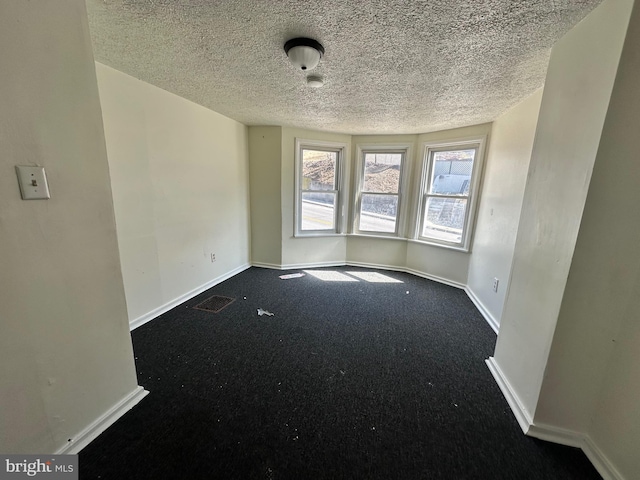 spare room featuring a textured ceiling, dark carpet, visible vents, and baseboards