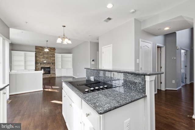 kitchen with dark wood-style flooring, white cabinetry, a stone fireplace, and black electric stovetop