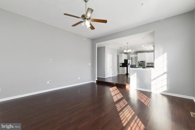 unfurnished living room with dark wood-style floors, baseboards, and ceiling fan with notable chandelier