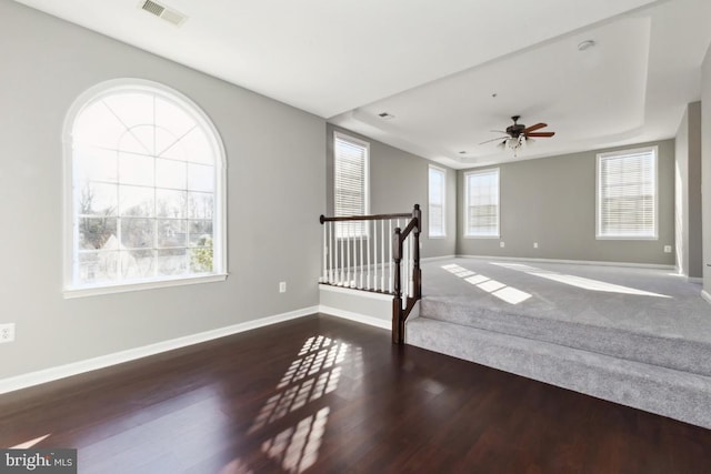 empty room featuring a ceiling fan, visible vents, baseboards, and wood finished floors