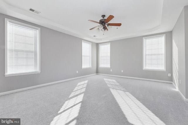 spare room with a tray ceiling, carpet, visible vents, ceiling fan, and baseboards