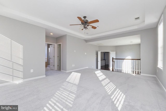 carpeted spare room with a ceiling fan, a raised ceiling, visible vents, and baseboards