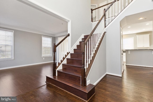 stairway with crown molding, a towering ceiling, baseboards, and wood finished floors