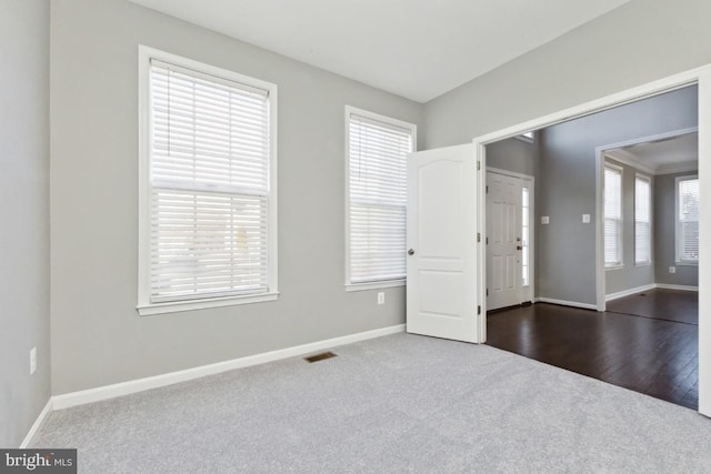 empty room with dark colored carpet, visible vents, and baseboards