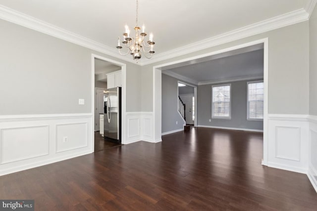 unfurnished dining area featuring dark wood-style flooring, crown molding, stairway, an inviting chandelier, and wainscoting