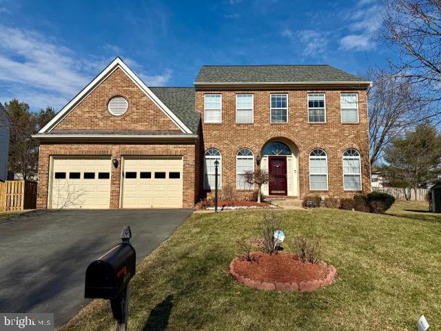 colonial inspired home with driveway, a garage, a shingled roof, a front lawn, and brick siding