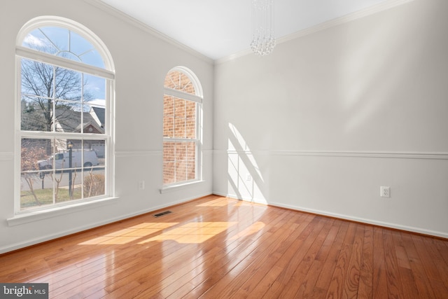 empty room featuring visible vents, a notable chandelier, ornamental molding, wood-type flooring, and baseboards