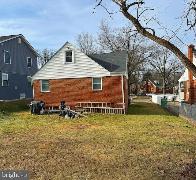 view of property exterior with brick siding, a lawn, and fence