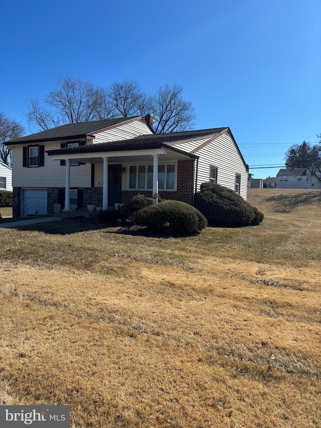 view of front of home with a front yard, covered porch, a chimney, and an attached garage