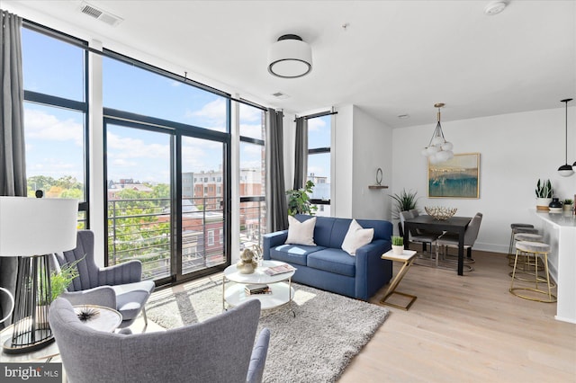 living area featuring baseboards, a wall of windows, visible vents, and light wood-style floors