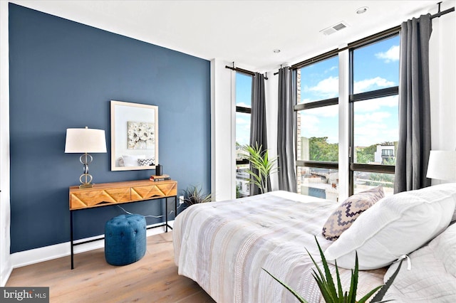 bedroom with a wall of windows, wood finished floors, visible vents, and baseboards