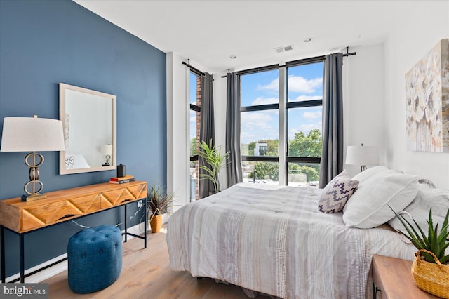 bedroom with floor to ceiling windows, visible vents, and wood finished floors