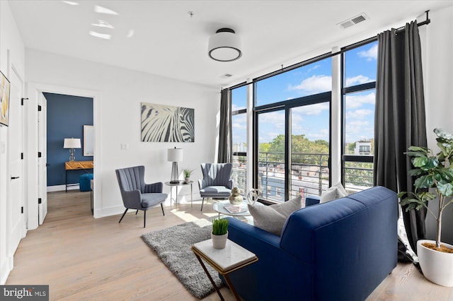 sitting room featuring light wood-type flooring, baseboards, expansive windows, and visible vents