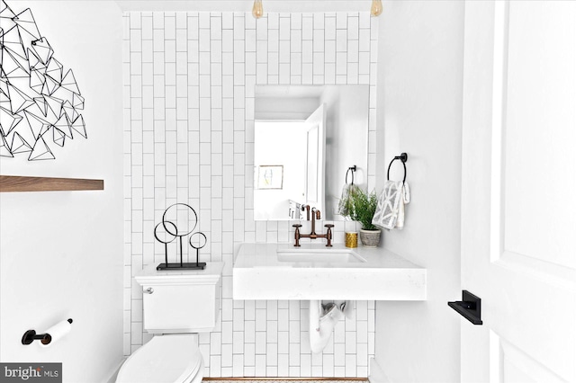 bathroom with a sink, tile walls, and toilet