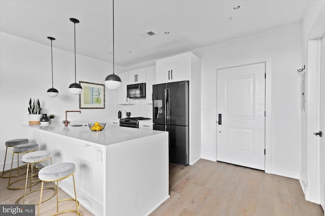 kitchen with a breakfast bar, light wood-style floors, a sink, a peninsula, and black appliances