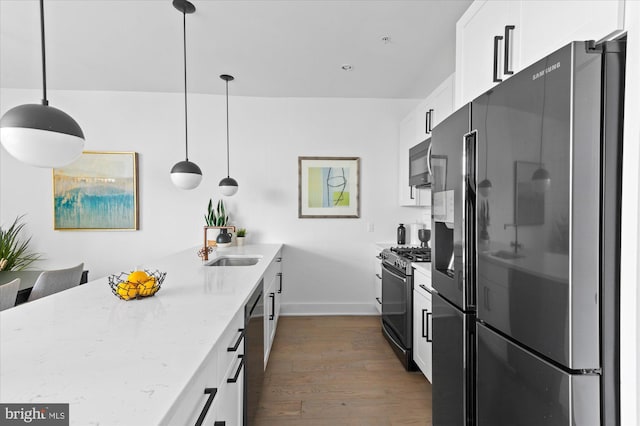 kitchen with white cabinets, dark wood finished floors, light stone countertops, stainless steel appliances, and a sink