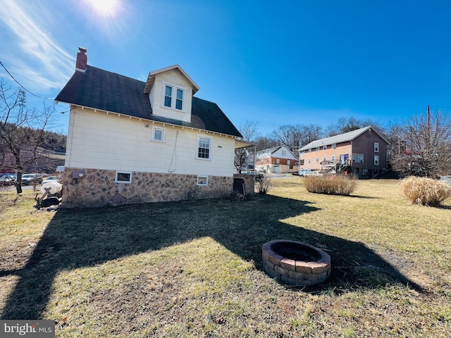 view of property exterior featuring an outdoor fire pit, a lawn, and a chimney