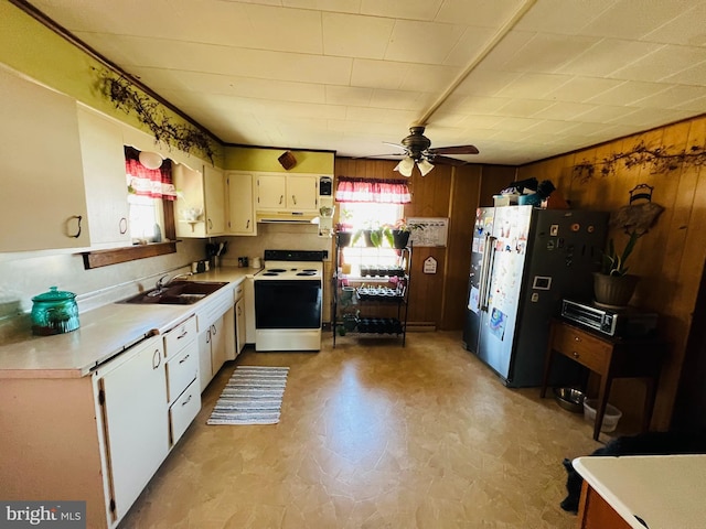 kitchen featuring white appliances, light countertops, wood walls, under cabinet range hood, and a sink