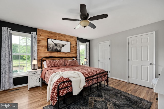 bedroom with baseboards, visible vents, ceiling fan, wood finished floors, and wood walls