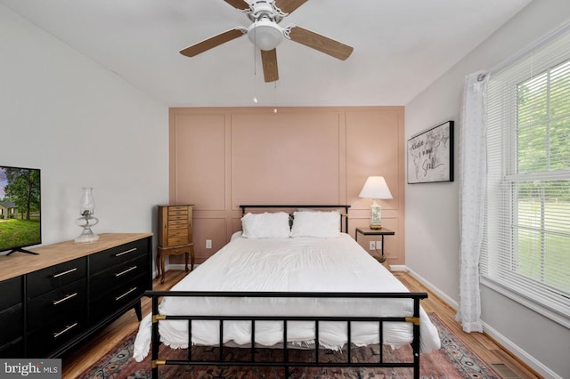 bedroom featuring light wood finished floors, visible vents, a decorative wall, ceiling fan, and baseboards