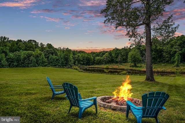 yard at dusk featuring a fire pit, a water view, and a wooded view