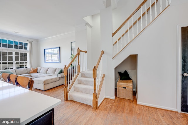 living area with visible vents, ornamental molding, light wood-type flooring, baseboards, and stairs