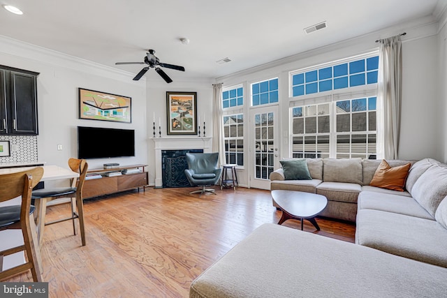 living area featuring a fireplace, light wood finished floors, visible vents, ornamental molding, and plenty of natural light