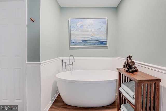 full bath with a soaking tub, wood finished floors, and wainscoting