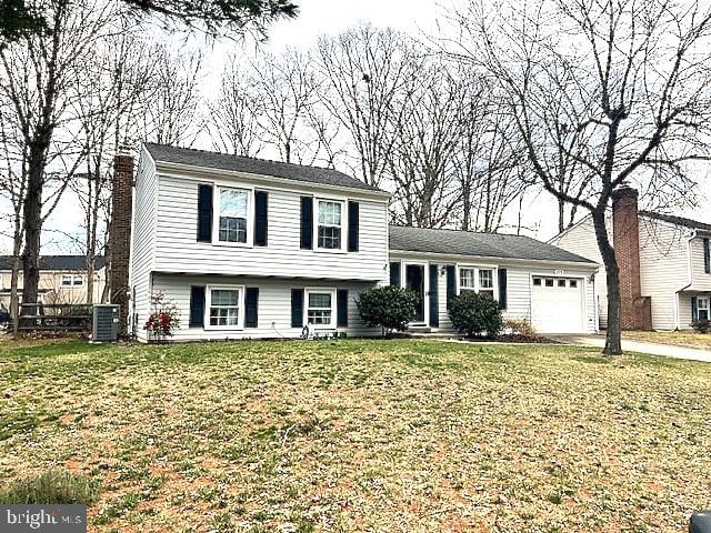 tri-level home featuring cooling unit, a garage, driveway, a chimney, and a front yard