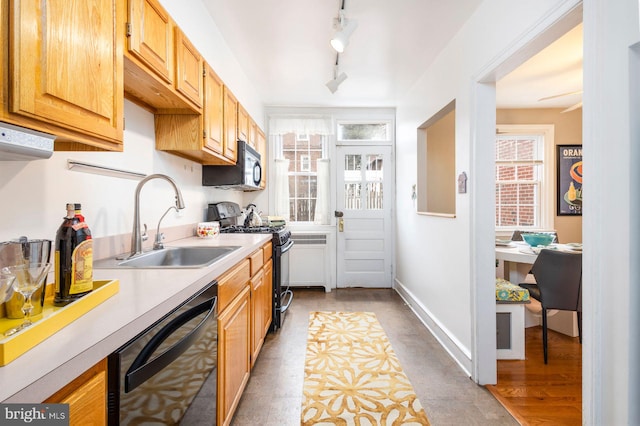 kitchen with light countertops, a sink, black appliances, track lighting, and baseboards