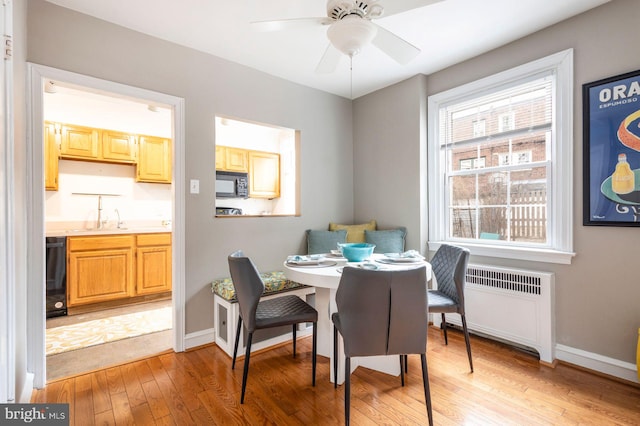 dining space featuring radiator heating unit, light wood-type flooring, a ceiling fan, and baseboards