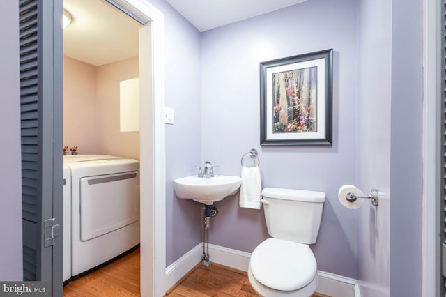 half bathroom featuring toilet, a sink, wood finished floors, baseboards, and washer / dryer