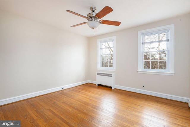 empty room featuring ceiling fan, radiator heating unit, light wood-type flooring, and baseboards