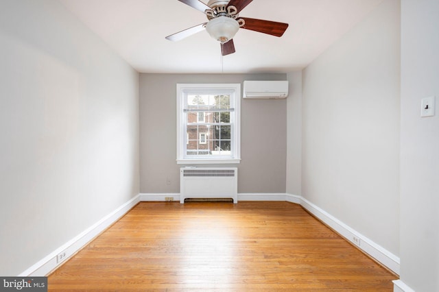 empty room with a wall unit AC, radiator, a ceiling fan, light wood-type flooring, and baseboards