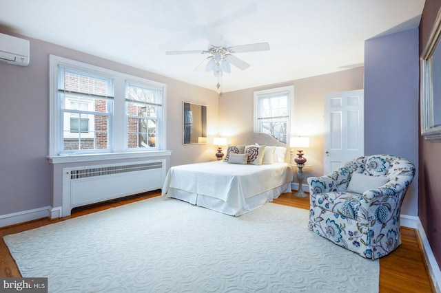 bedroom with wood finished floors, a ceiling fan, baseboards, radiator, and a wall mounted air conditioner