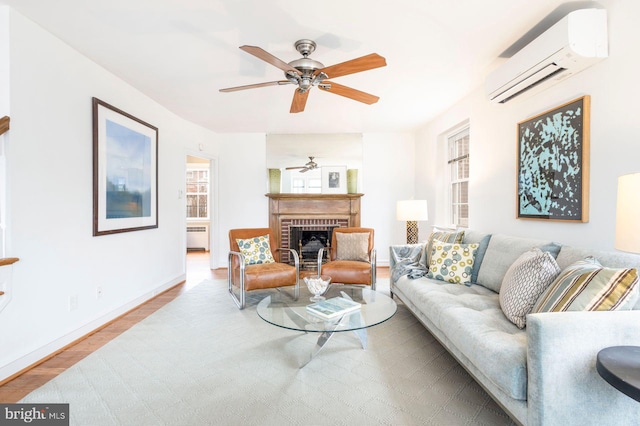 living room with baseboards, ceiling fan, wood finished floors, a brick fireplace, and a wall mounted AC