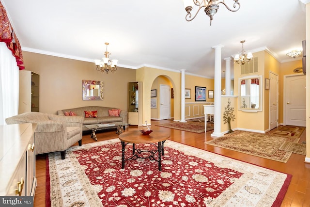 living room with ornate columns, ornamental molding, wood finished floors, and an inviting chandelier