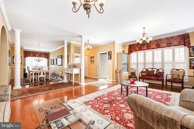 living area featuring a healthy amount of sunlight, an inviting chandelier, decorative columns, and hardwood / wood-style floors