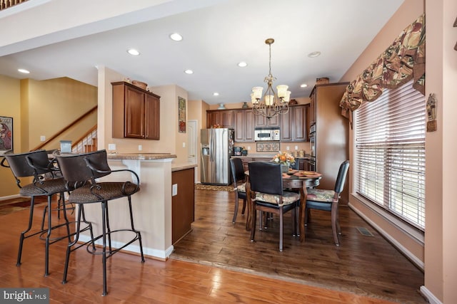 kitchen with dark wood finished floors, a notable chandelier, stainless steel appliances, a peninsula, and a kitchen bar