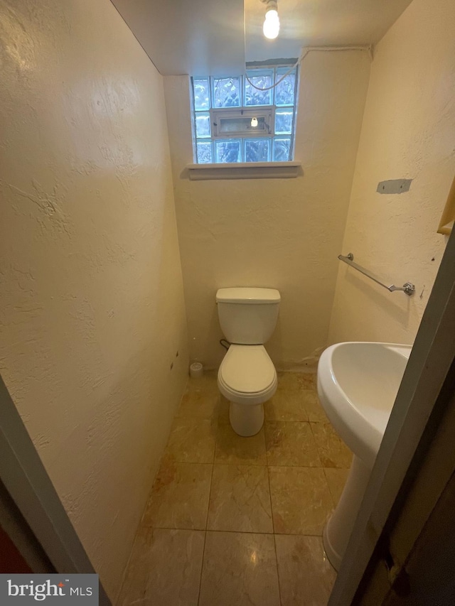 bathroom with a textured wall, tile patterned flooring, and toilet