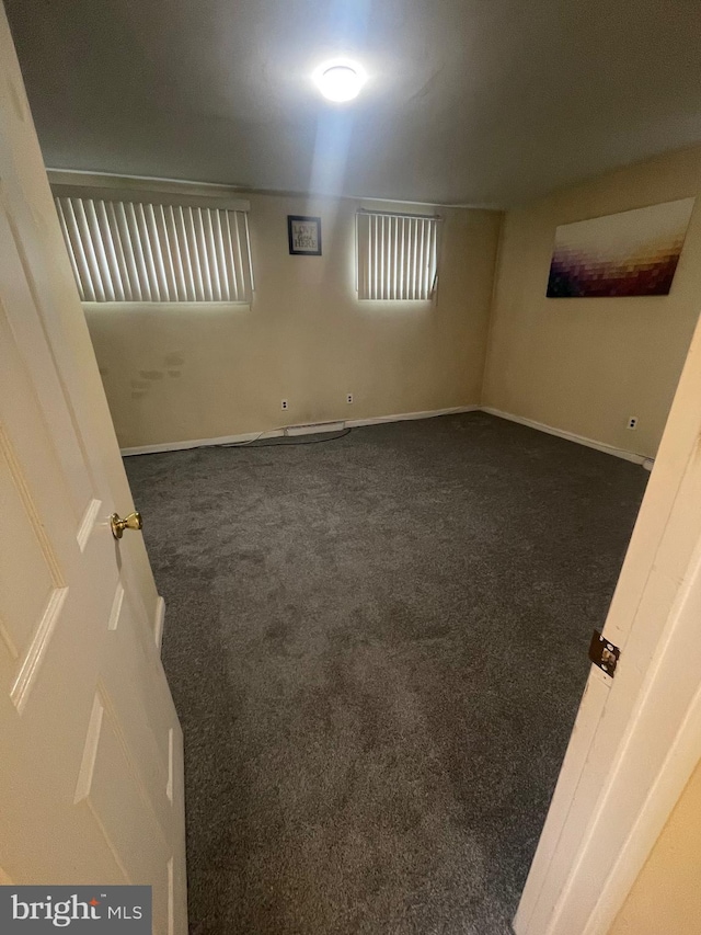 empty room featuring dark colored carpet and baseboards